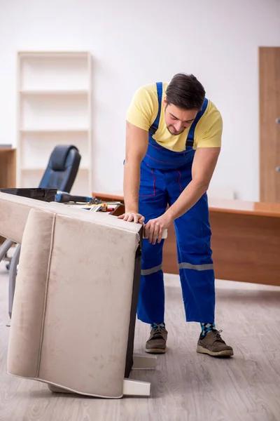 Genç erkek marangoz ofiste kol sandalyesini tamir ediyor. — Stok fotoğraf