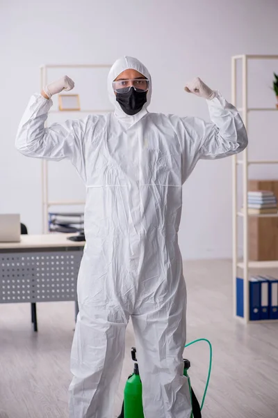 Młody mężczyzna wykonawca odkażający biuro podczas pandemii — Zdjęcie stockowe