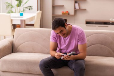 Genç adam salgın sırasında evde televizyon izliyor.