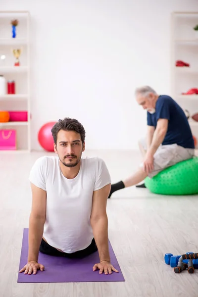 Genç erkek eğitmen ve yaşlı adam spor yapıyor. — Stok fotoğraf