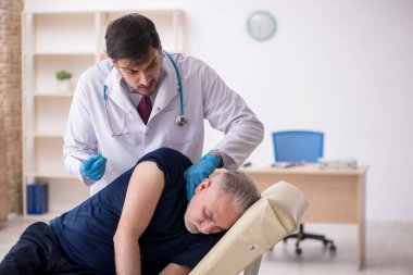 Yaşlı bir erkek hasta aşıyla genç bir doktoru ziyaret ediyor.