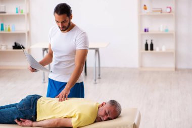 Yaşlı erkek hasta, genç erkek doktor masörünü ziyaret ediyor.