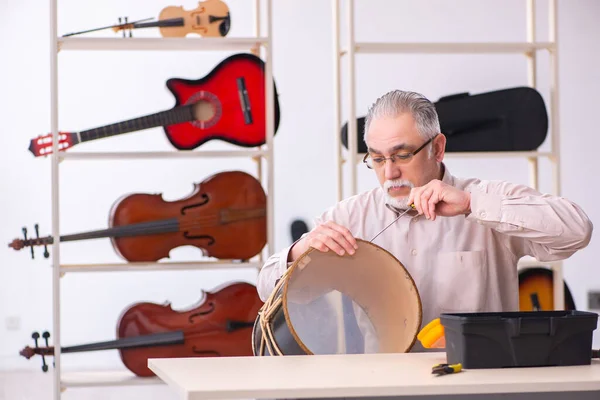 Oude mannelijke reparateur repareert muziekinstrumenten op het werk — Stockfoto