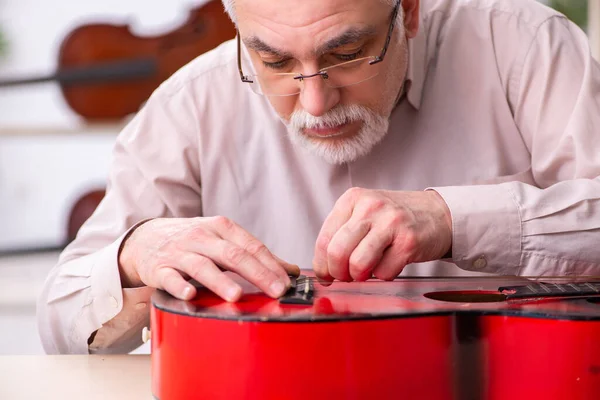 Alte männliche Reparaturkraft repariert Musikinstrumente am Arbeitsplatz — Stockfoto