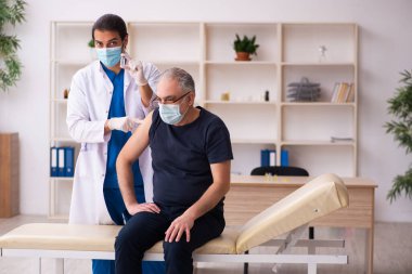 Yaşlı adam covid-19 aşı konseptinde genç doktoru ziyaret ediyor.