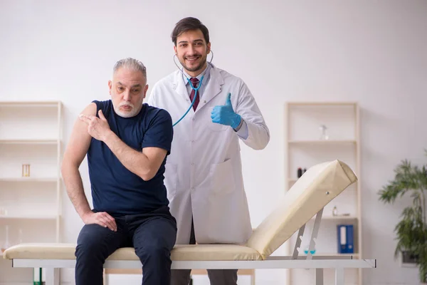 Paciente do sexo masculino idoso visitando jovem médico do sexo masculino em conce vacinação — Fotografia de Stock