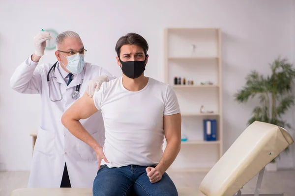 Paciente masculino joven que visita a un viejo médico en concepto de vacunación — Foto de Stock