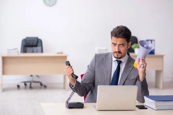 Young male employee holding megaphone at workplace — Stock Photo, Image