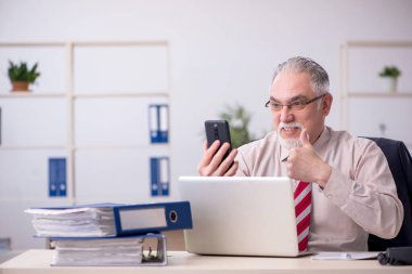 Eski erkek çalışan işyerinde oturuyor.