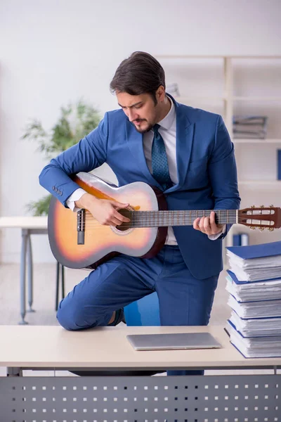 Mladý muž zaměstnanec hraje na kytaru na pracovišti — Stock fotografie