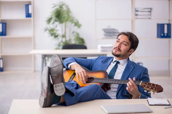 Jeune employé masculin jouant de la guitare sur le lieu de travail — Photo