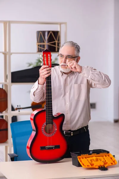 Oude mannelijke reparateur repareert muziekinstrumenten op het werk — Stockfoto