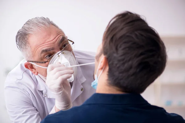 Jonge mannelijke patiënt bezoekt oude mannelijke arts tijdens pandemie — Stockfoto