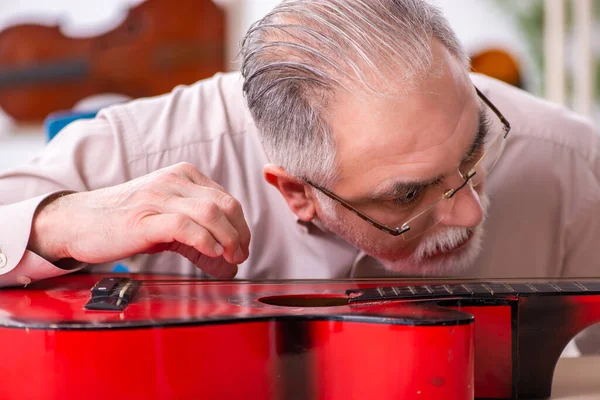 Alte männliche Reparaturkraft repariert Musikinstrumente am Arbeitsplatz — Stockfoto