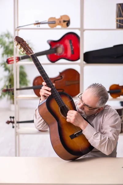 Oude mannelijke reparateur repareert muziekinstrumenten op het werk — Stockfoto