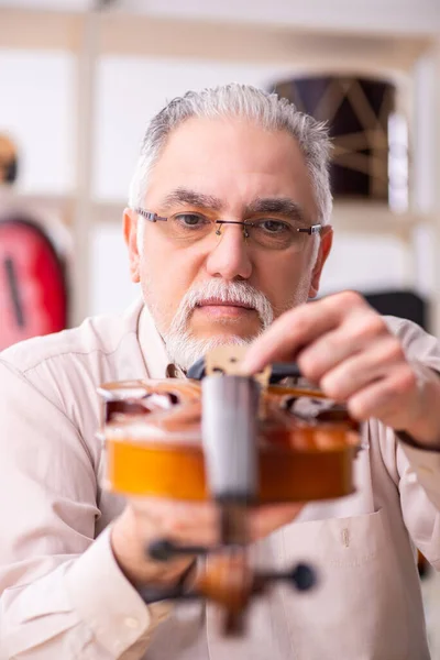 Oude mannelijke reparateur repareert muziekinstrumenten op het werk — Stockfoto