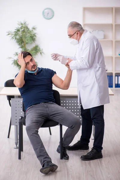 Genç erkek hasta yaşlı erkek doktoru aşıyla ziyaret ediyor. — Stok fotoğraf