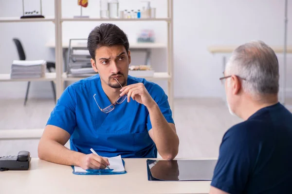 Homem velho visitando jovem médico masculino — Fotografia de Stock