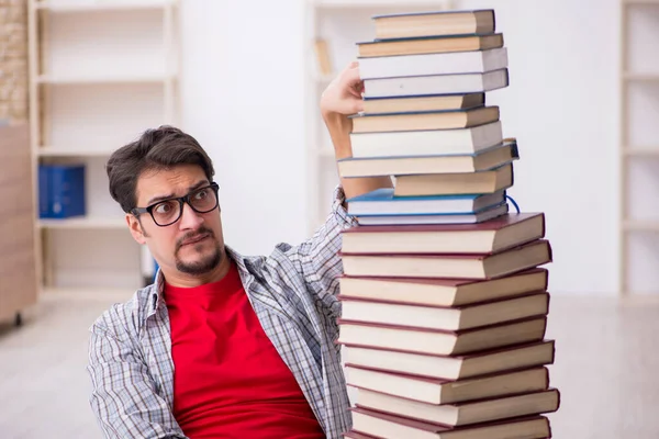 Mladý muž student a příliš mnoho knih ve třídě — Stock fotografie