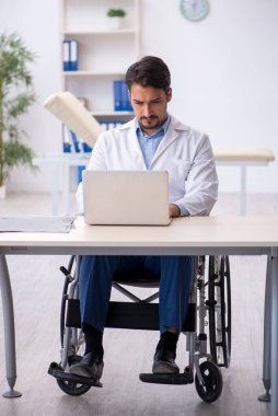 Klinikte çalışan tekerlekli sandalyedeki genç erkek doktor.
