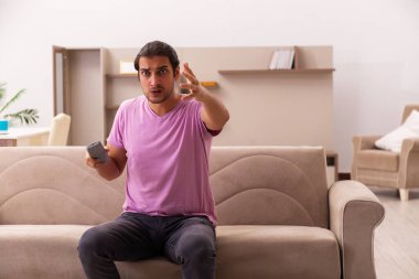 Genç adam salgın sırasında evde televizyon izliyor.