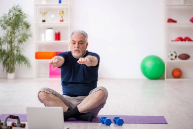 Yaşlı adam içeride spor egzersizleri yapıyor.