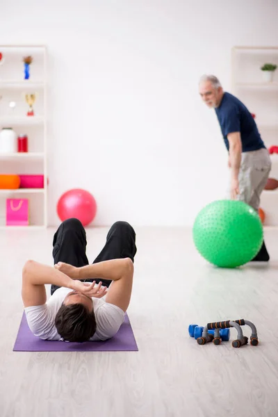 Genç erkek eğitmen ve yaşlı adam spor yapıyor. — Stok fotoğraf