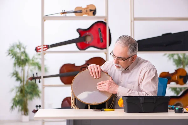 Oude mannelijke reparateur repareert muziekinstrumenten op het werk — Stockfoto