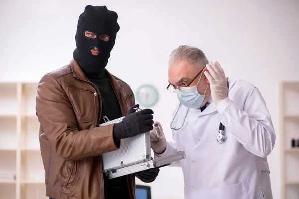 Masked man burglar bribing old doctor for getting vaccine