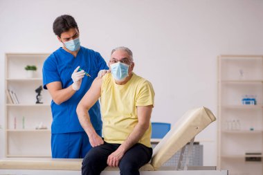 Yaşlı erkek hasta aşılama bölümünde genç bir erkek doktor.