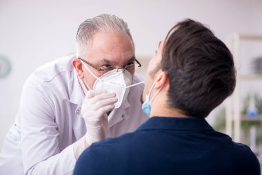 Genç erkek hasta salgın sırasında yaşlı erkek doktoru ziyaret ediyor.