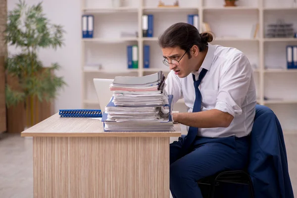 Ung manlig anställd och mycket arbete på kontoret — Stockfoto