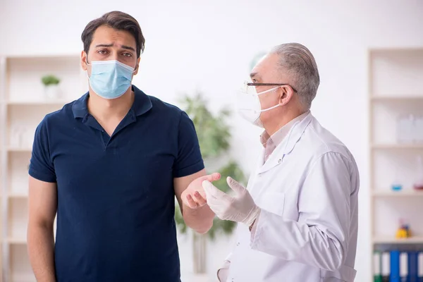 Junge männliche Patientin besucht alten Arzt während Pandemie — Stockfoto