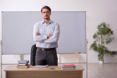 Genç erkek öğretmen beyaz tahtanın önünde.