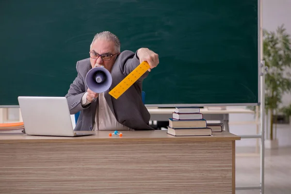 Old male teacher holding megaphone in front of blackboard — Stock Photo, Image