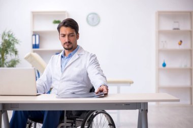 Klinikte çalışan tekerlekli sandalyedeki genç erkek doktor.