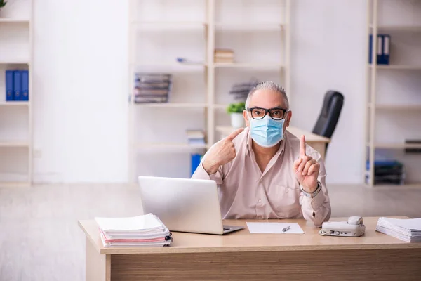 Gammel mannlig ansatt som arbeider på arbeidsplassen under pandemi – stockfoto