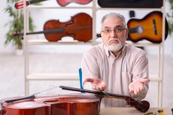 Old male repairman repairing musical instruments at workplace — Stock Photo, Image