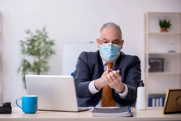 Velho funcionário do sexo masculino que trabalha no escritório durante pandemia — Fotografia de Stock