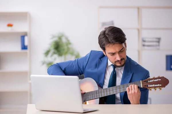 Joven empleado masculino tocando guitarra en el lugar de trabajo — Foto de Stock