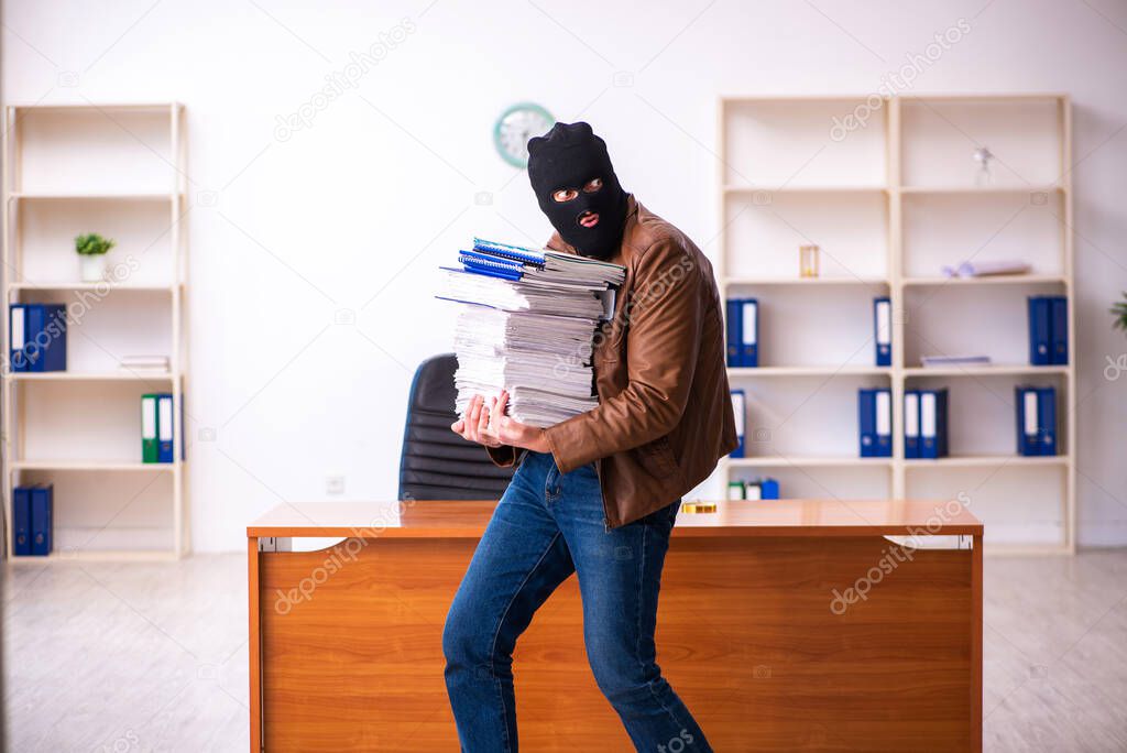 Young man in balaclava stealing information from the office