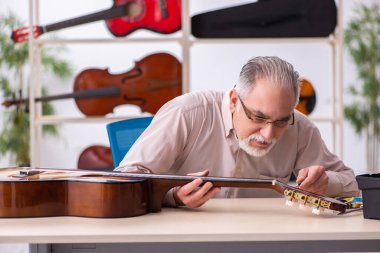 Yaşlı erkek tamirci iş yerinde müzik aletlerini tamir ediyor.