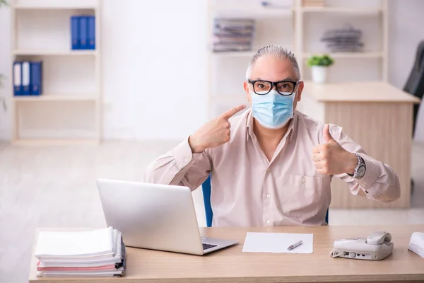 Velho empregado do sexo masculino que trabalha no local de trabalho durante a pandemia — Fotografia de Stock