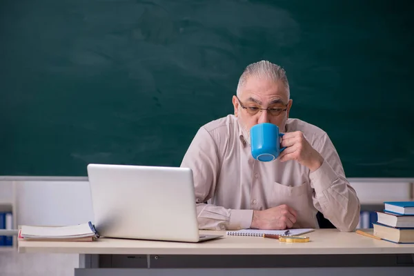 Old male teacher drinking coffee in the classroom