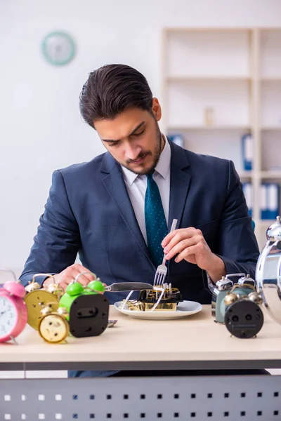 Junger Geschäftsmann isst Wecker — Stockfoto