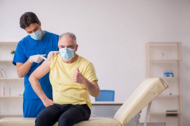 Yaşlı erkek hasta aşılama bölümünde genç bir erkek doktor.