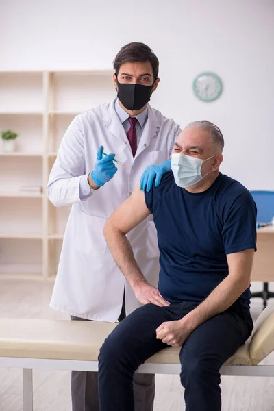 Oude mannelijke patiënt op bezoek bij jonge mannelijke arts in vaccinatiecentrum — Stockfoto