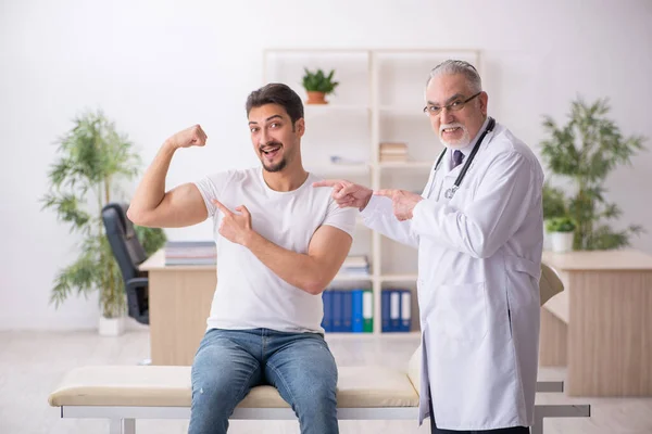 Jovem paciente masculino visitando velho médico masculino — Fotografia de Stock