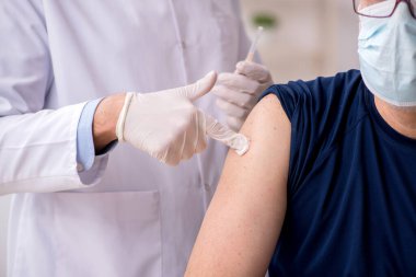 Yaşlı bir erkek hasta aşıyla genç bir doktoru ziyaret ediyor.