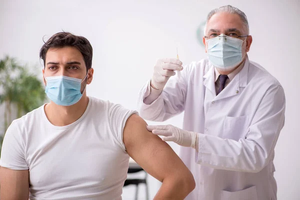 Giovane paziente di sesso maschile visita vecchio medico di sesso maschile in conce vaccinazione — Foto Stock